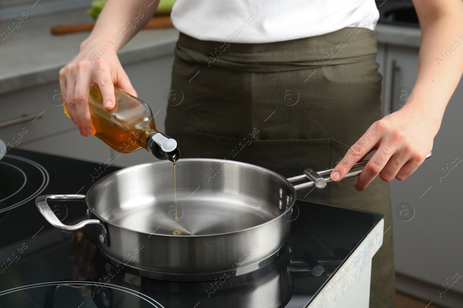 Photo of Vegetable fats. Woman pouring oil into frying pan on cooktop in kitchen, closeup