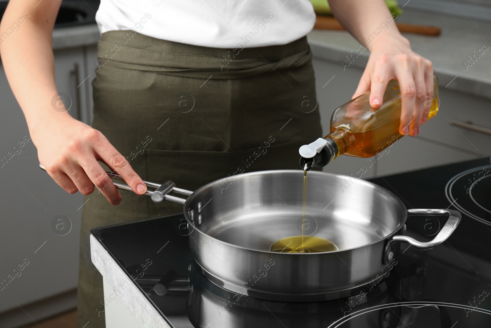 Photo of Vegetable fats. Woman pouring oil into frying pan on cooktop in kitchen, closeup