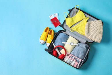 Photo of Open suitcase with traveler's belongings on light blue background, flat lay. Space for text