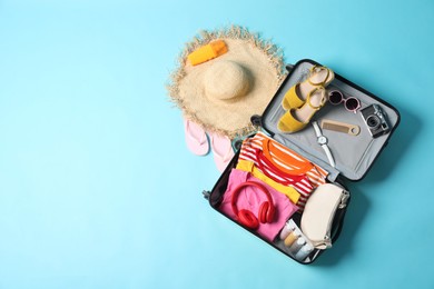 Open suitcase with traveler's belongings on light blue background, flat lay. Space for text