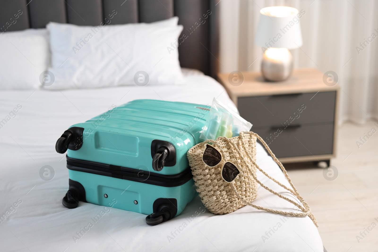 Photo of Turquoise suitcase, bag, sunglasses and cosmetic travel kit on bed indoors