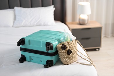 Turquoise suitcase, bag, sunglasses and cosmetic travel kit on bed indoors