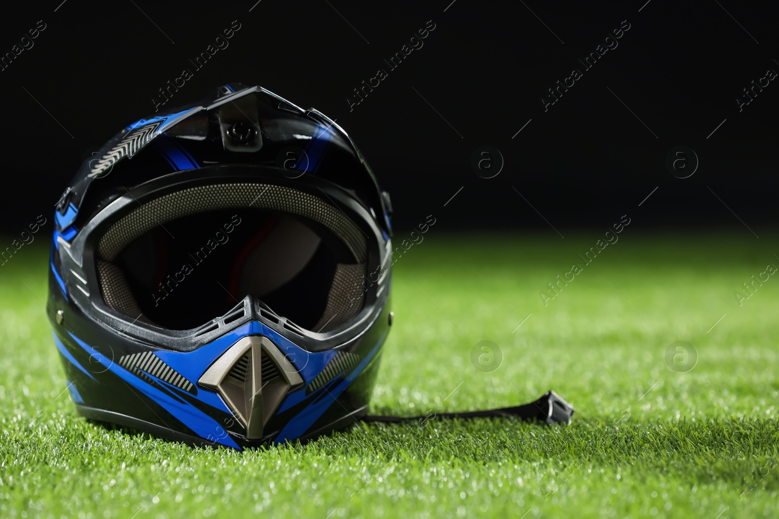 Photo of Modern motorcycle helmet with visor on green grass against black background, space for text