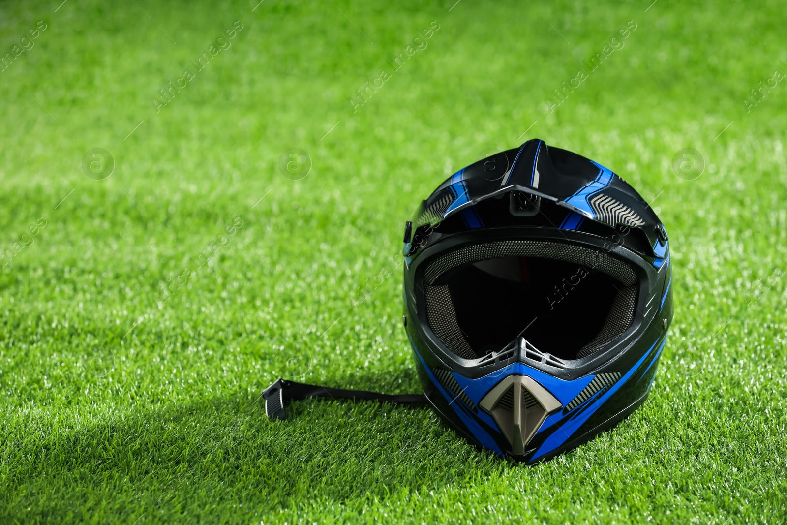 Photo of Modern motorcycle helmet with visor on green grass, space for text