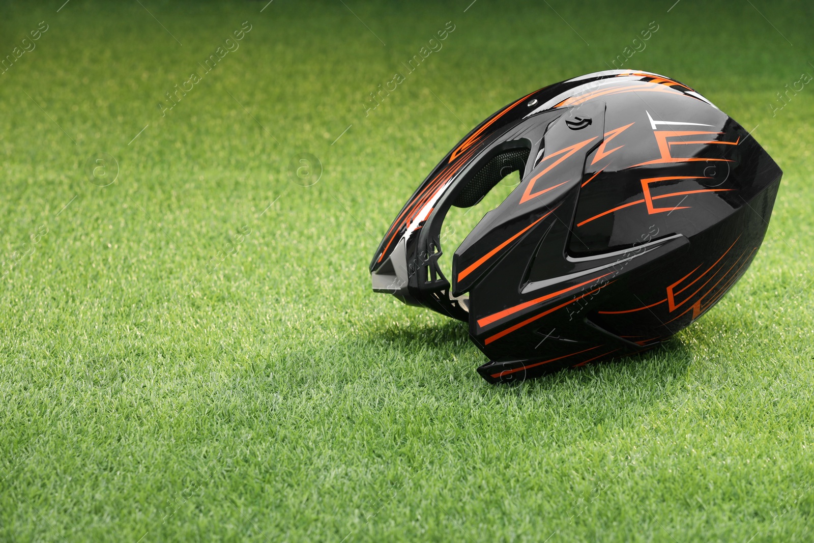 Photo of Modern motorcycle helmet with visor on green grass, space for text