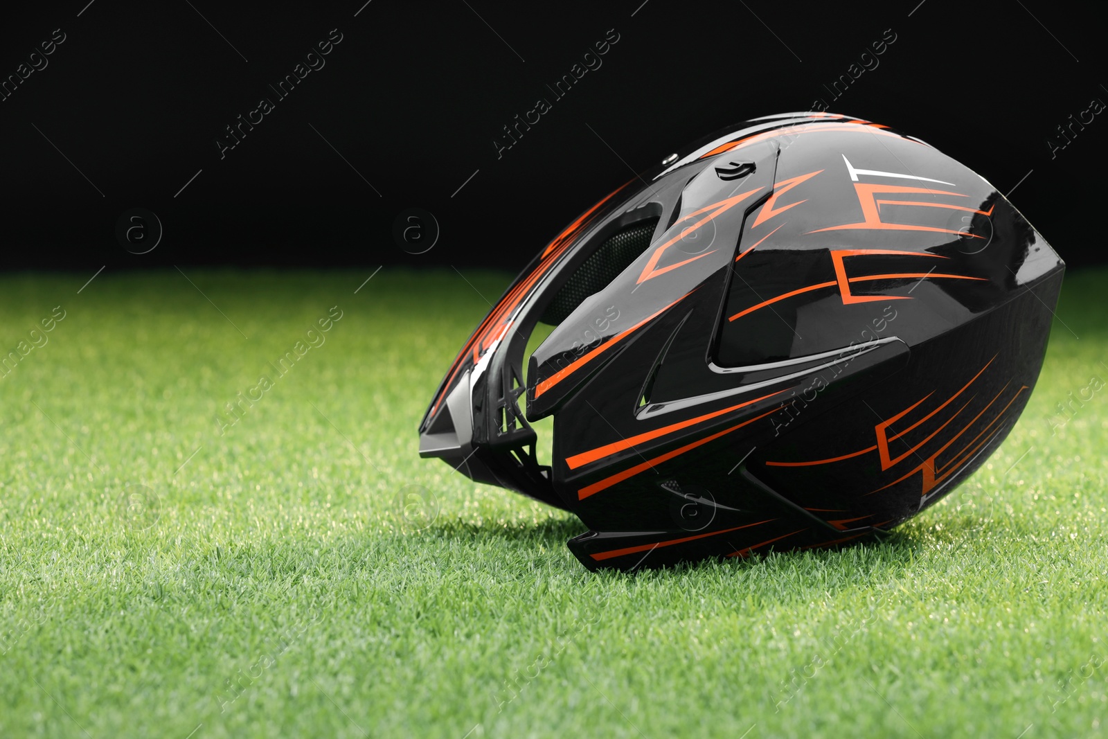 Photo of Modern motorcycle helmet with visor on green grass against black background, space for text