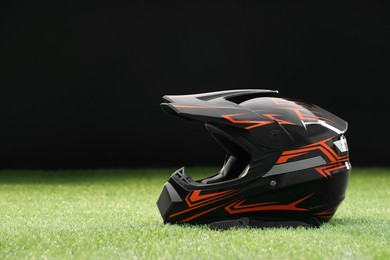 Photo of Modern motorcycle helmet with visor on green grass against black background, space for text