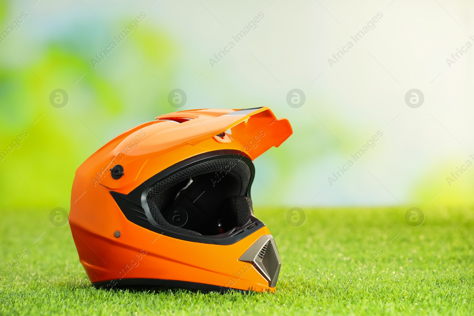 Photo of Orange motorcycle helmet with visor on green grass, space for text