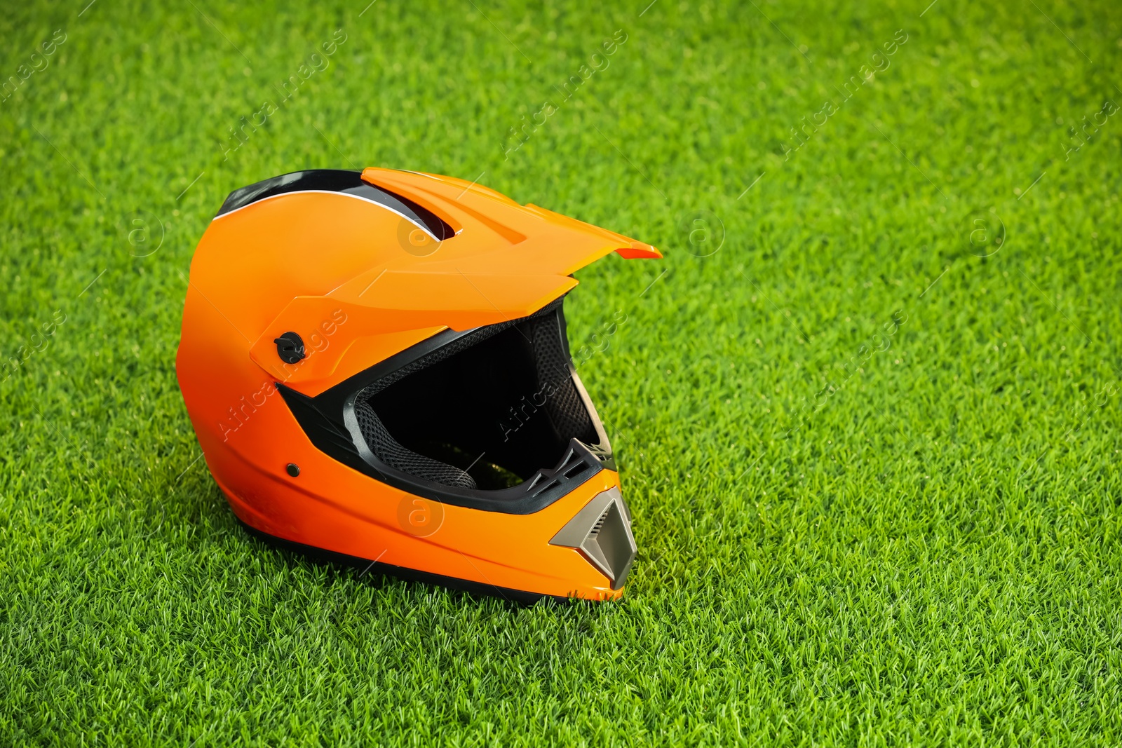 Photo of Orange motorcycle helmet with visor on green grass, space for text