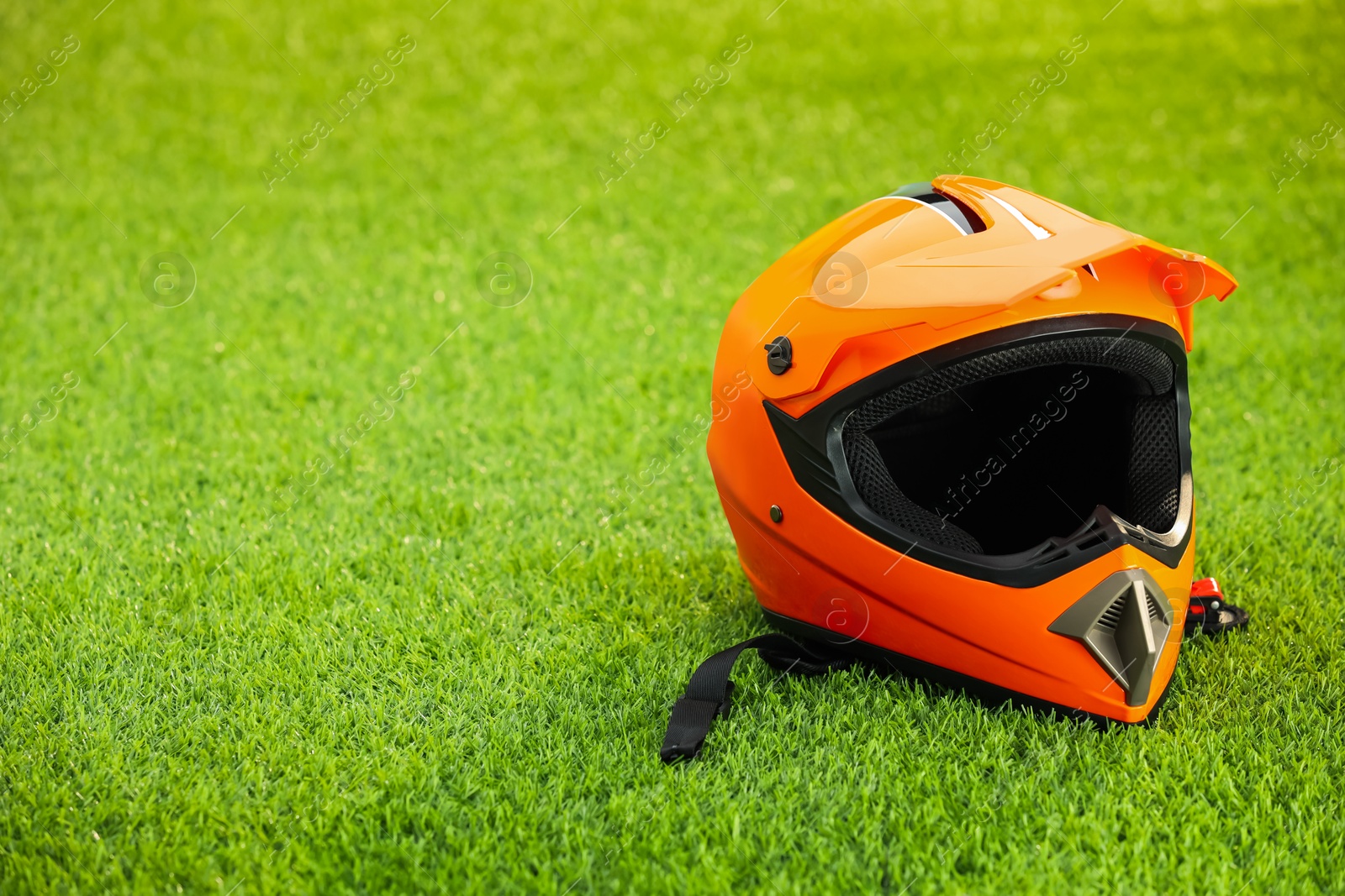 Photo of Orange motorcycle helmet with visor on green grass, space for text