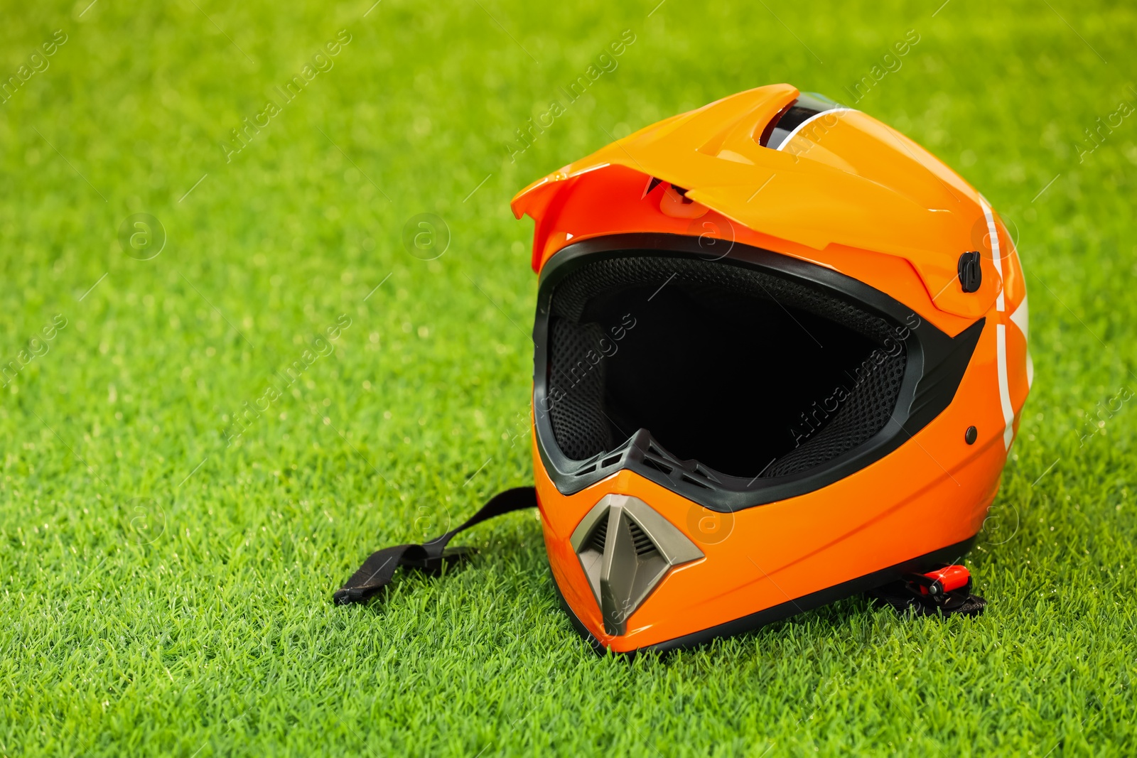 Photo of Orange motorcycle helmet with visor on green grass, space for text