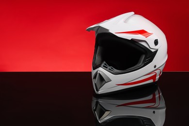 Photo of Modern motorcycle helmet with visor on mirror surface against red background. Space for text