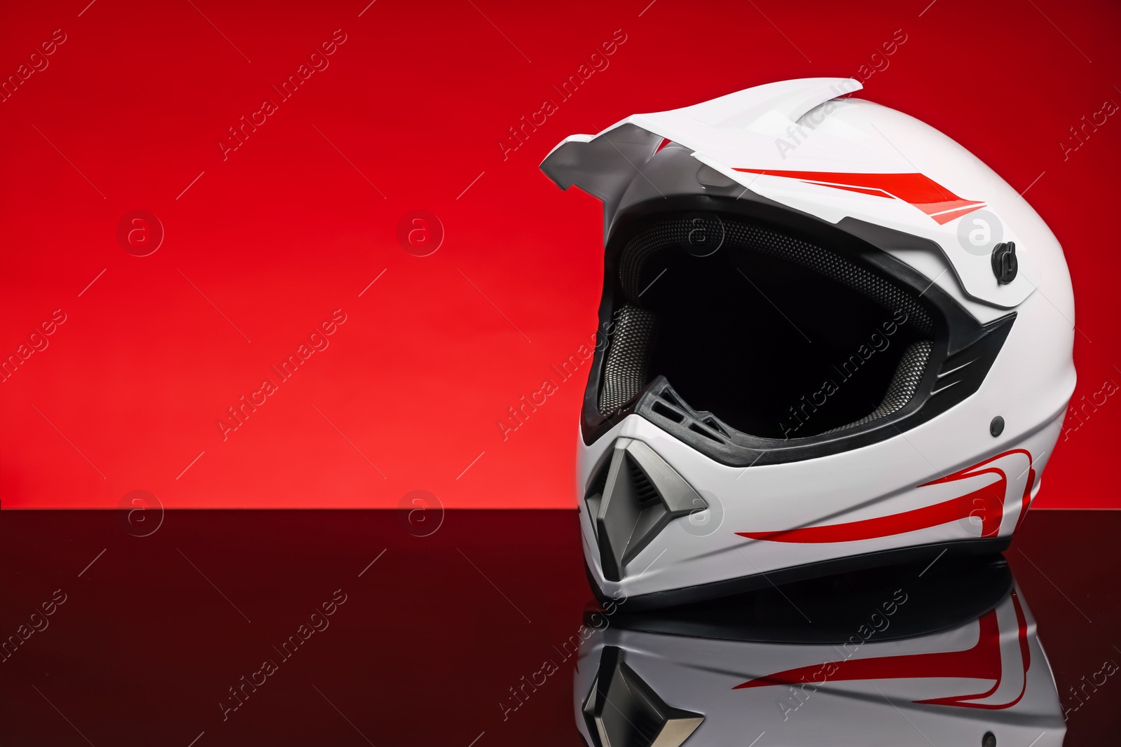 Photo of Modern motorcycle helmet with visor on mirror surface against red background. Space for text