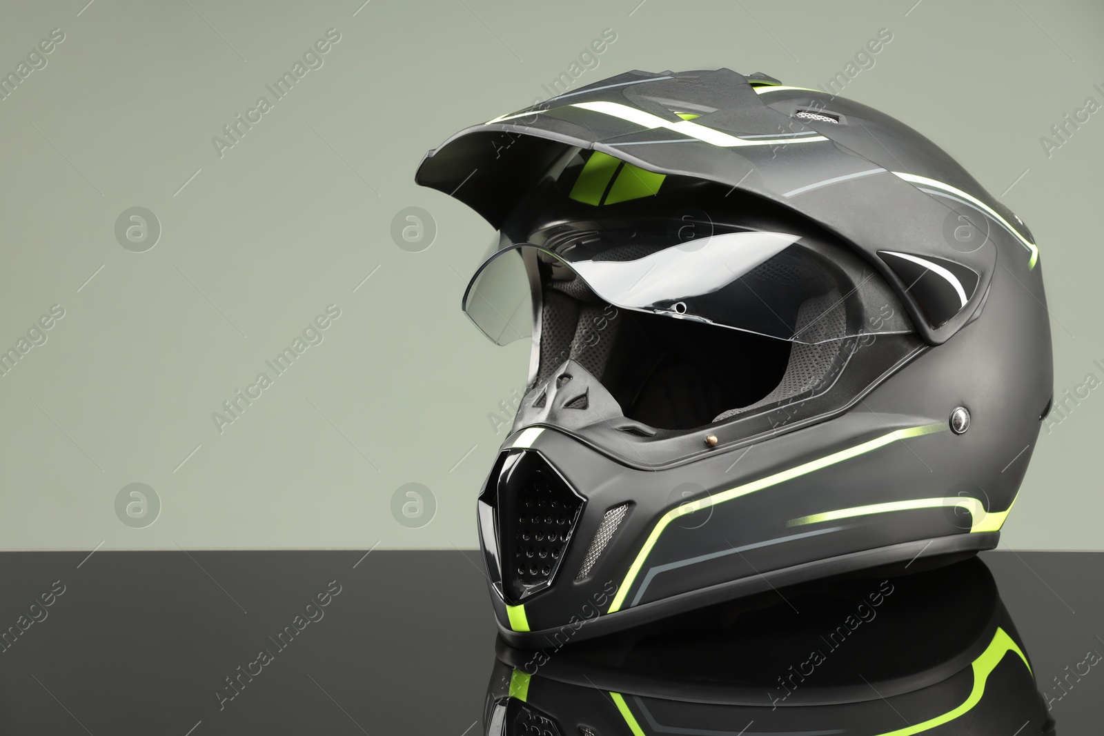 Photo of Modern motorcycle helmet with visor on mirror surface against light grey background. Space for text