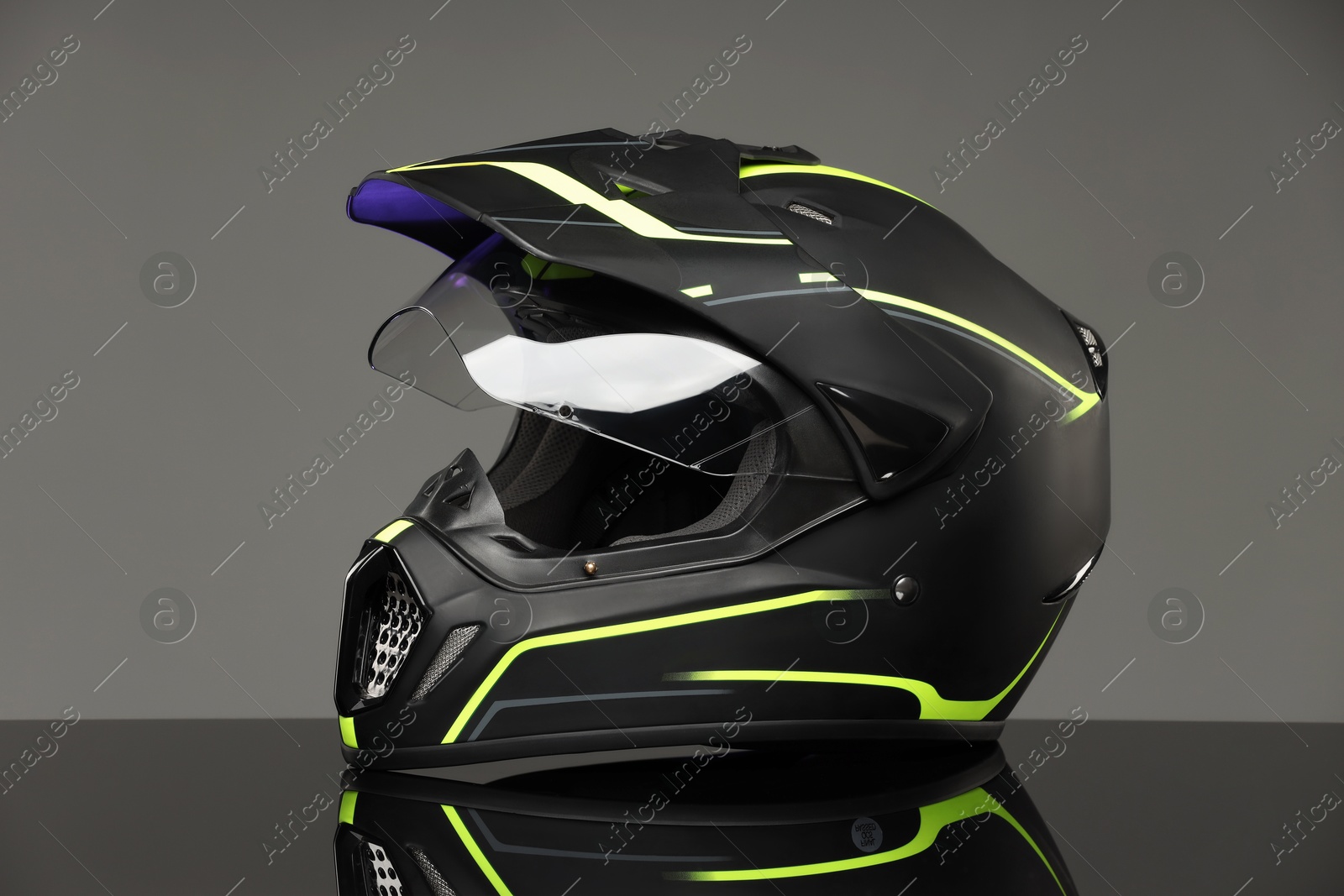 Photo of Modern motorcycle helmet with visor on mirror surface against light grey background