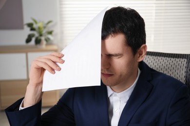 Photo of Embarrassed young man with document in office
