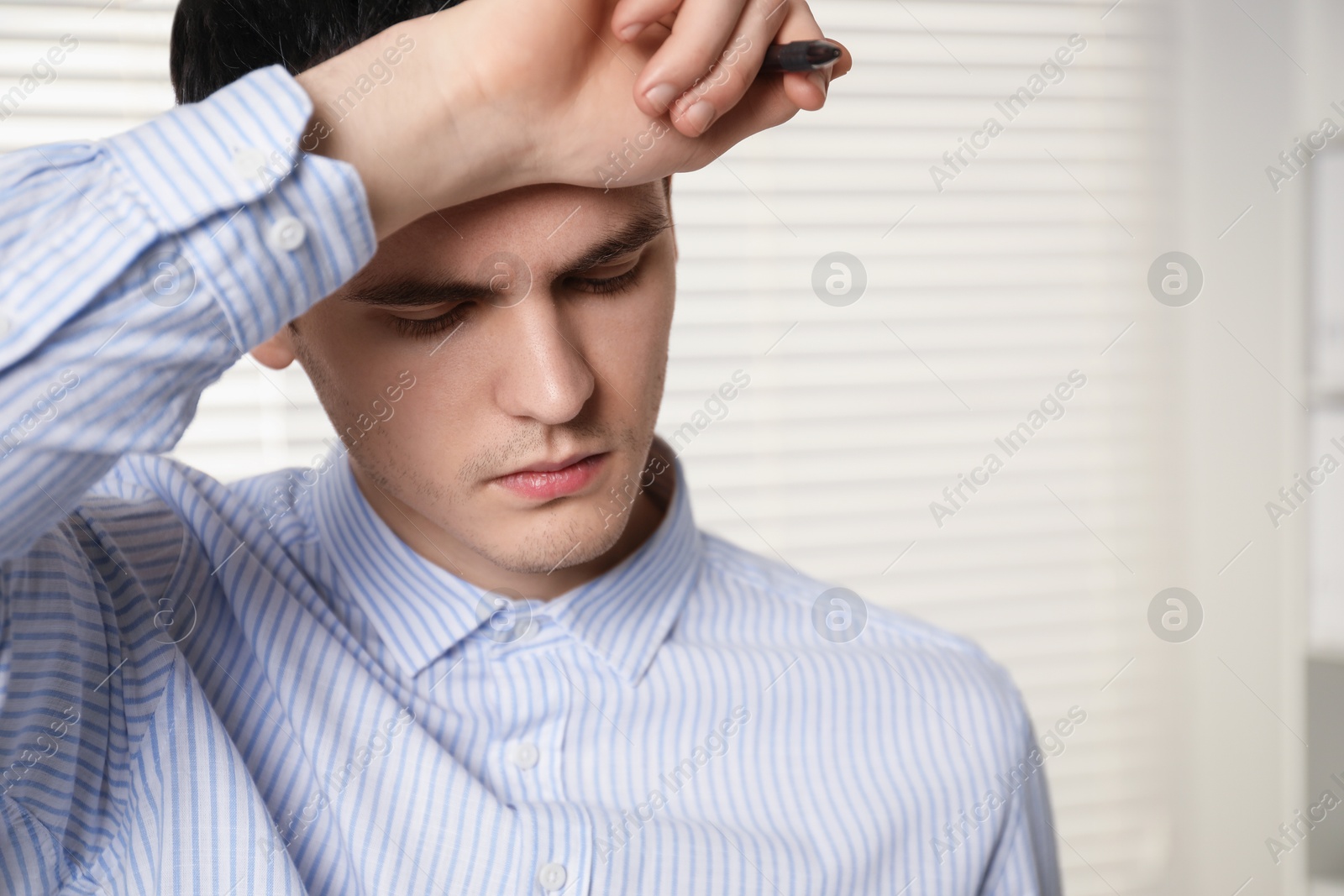 Photo of Embarrassed young man with pen in office. Space for text