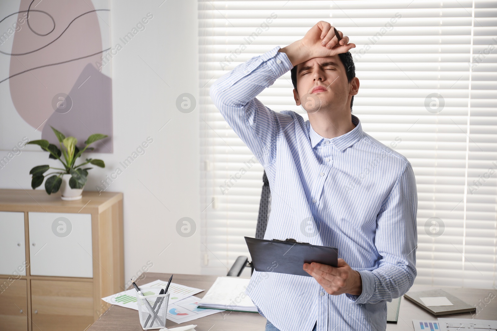 Photo of Embarrassed man with clipboard and pen in office, space for text