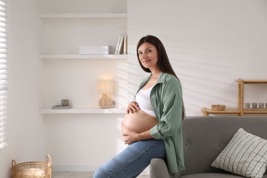 Photo of Beautiful pregnant woman sitting on sofa at home