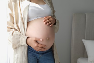 Photo of Pregnant woman in beige shirt at home, closeup