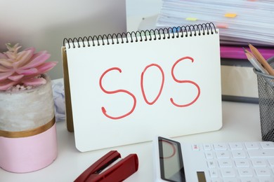 Photo of Notebook with word SOS and stationery on white table at workplace