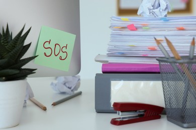 Photo of Note with word SOS and stationery on white table at workplace