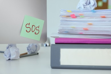 Note with word SOS and stationery on white table at workplace