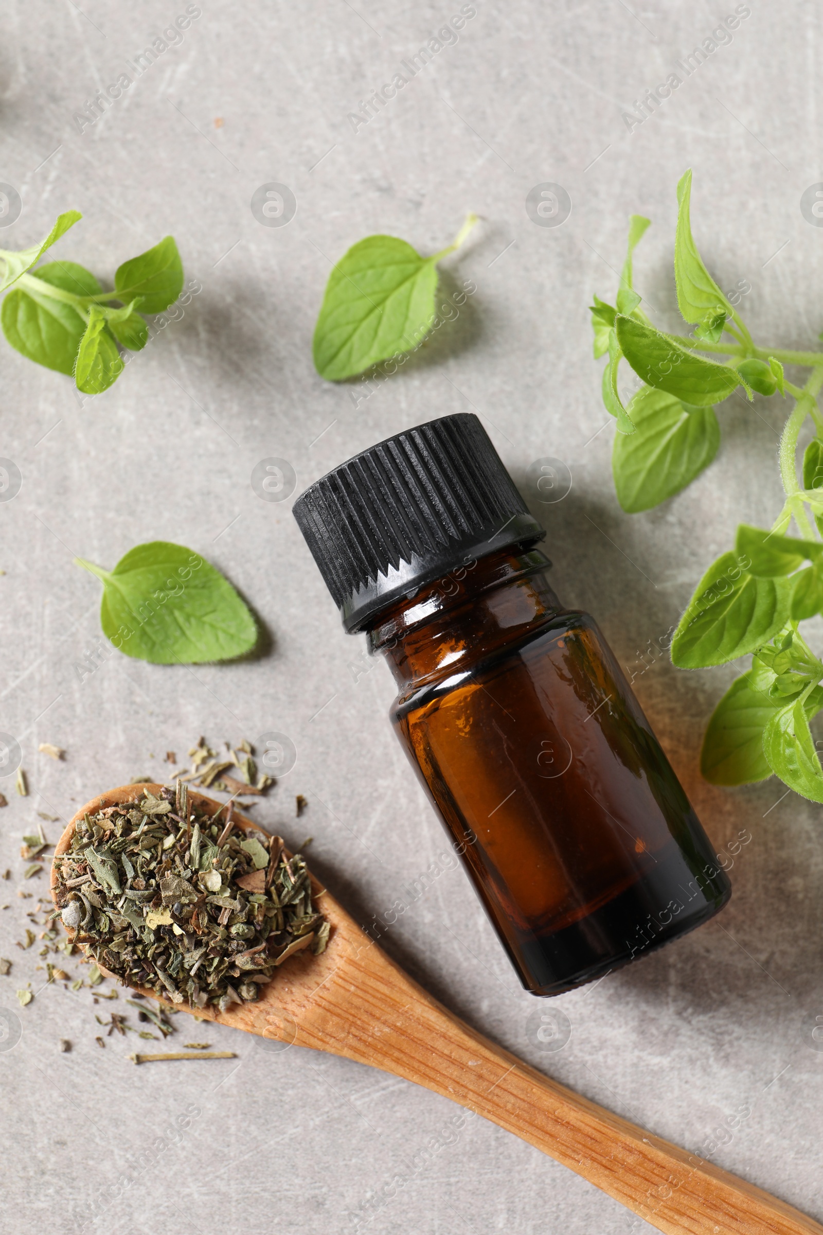 Photo of Essential oil in bottle, dry herb and oregano leaves on light grey textured table, flat lay