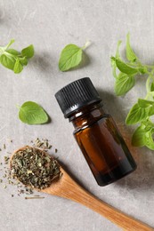 Essential oil in bottle, dry herb and oregano leaves on light grey textured table, flat lay