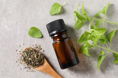 Essential oil in bottle, dry herb and oregano leaves on light grey textured table, flat lay