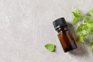 Essential oil in bottle and oregano leaves on light grey textured table, flat lay. Space for text