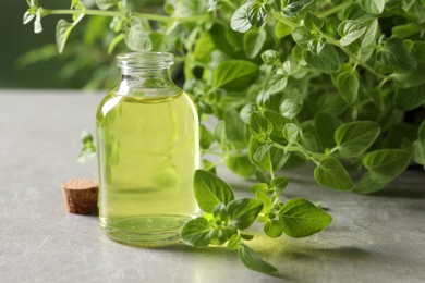 Photo of Essential oil in bottle and oregano twigs on light grey textured table, closeup