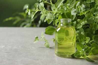 Photo of Essential oil in bottle and oregano twigs on light grey textured table against blurred green background, closeup. Space for text