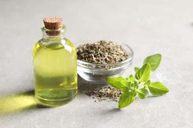 Essential oil in bottle, dry herb and oregano leaves on light grey textured table, closeup