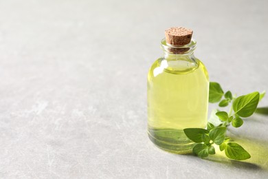 Photo of Essential oil in bottle and oregano twig on light grey textured table, closeup. Space for text