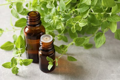 Photo of Essential oil in bottles and oregano twigs on light grey textured table, closeup