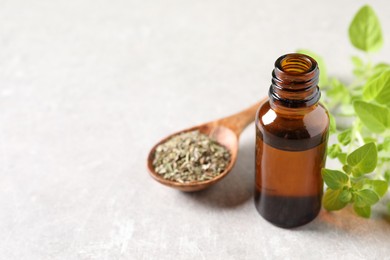 Photo of Essential oil in bottle, spoon with dry herb and oregano twigs on light textured table, closeup. Space for text