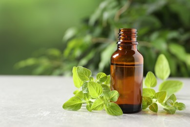 Essential oil in bottle and oregano twigs on light textured table against blurred green background, closeup. Space for text