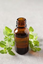 Essential oil in bottle and oregano twigs on light textured table, closeup