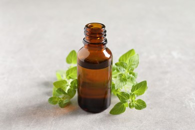 Essential oil in bottle and oregano twigs on light textured table, closeup