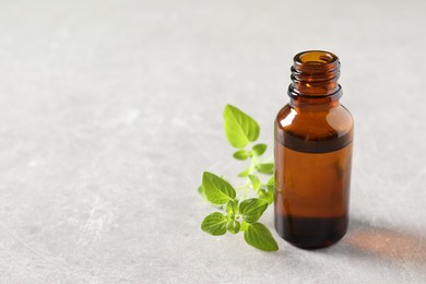 Photo of Essential oil in bottle and oregano twigs on light textured table, closeup. Space for text