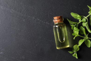 Photo of Essential oil in bottle and oregano twigs on dark textured table, flat lay. Space for text