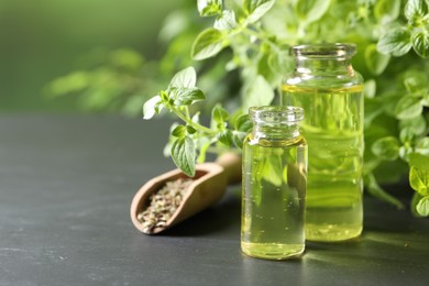 Photo of Essential oil in bottles and oregano twigs on dark textured table against blurred green background, closeup. Space for text