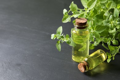 Photo of Essential oil in bottles and oregano twigs on dark textured table, closeup. Space for text