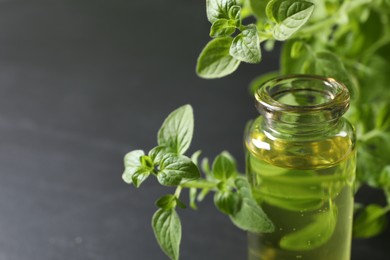 Photo of Essential oil in bottle and oregano twigs on grey background, closeup. Space for text