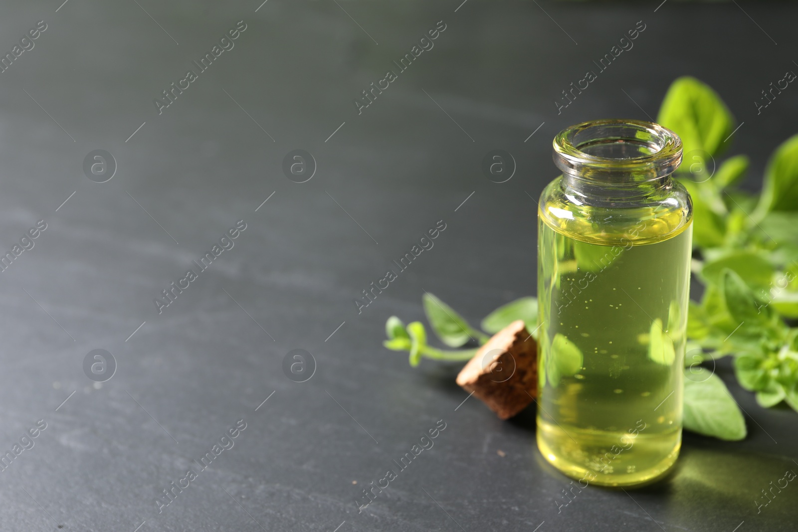 Photo of Essential oil in bottle and oregano twigs on dark textured table, closeup. Space for text