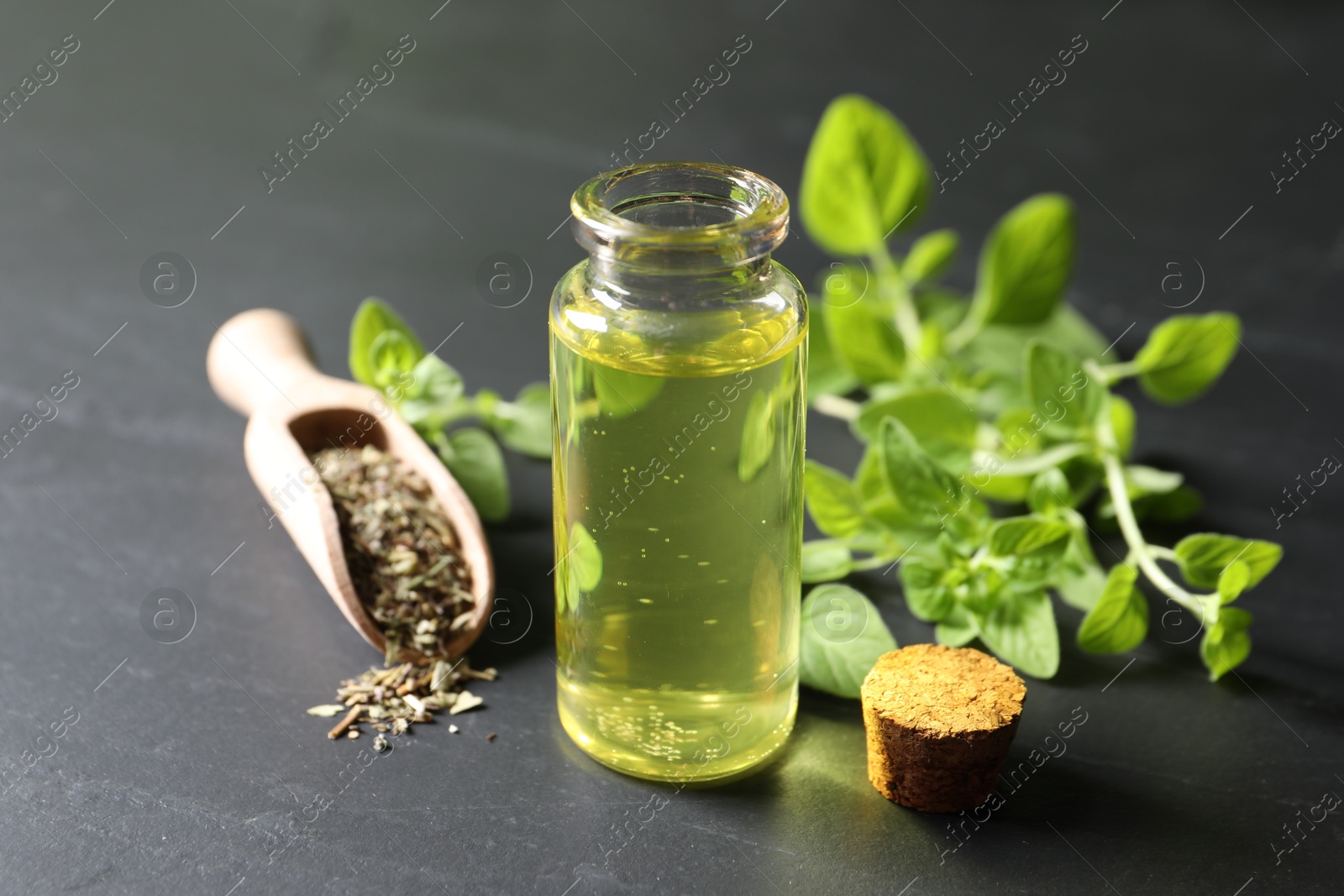 Photo of Essential oil in bottle, scoop with dry herb and oregano twigs on dark textured table, closeup