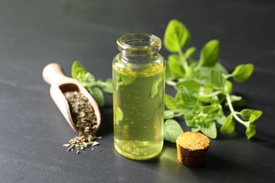 Photo of Essential oil in bottle, scoop with dry herb and oregano twigs on dark textured table, closeup