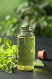 Essential oil in bottle and oregano twigs on dark textured table, closeup