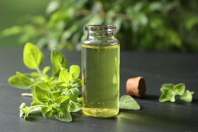 Photo of Essential oil in bottle and oregano twigs on dark textured table, closeup